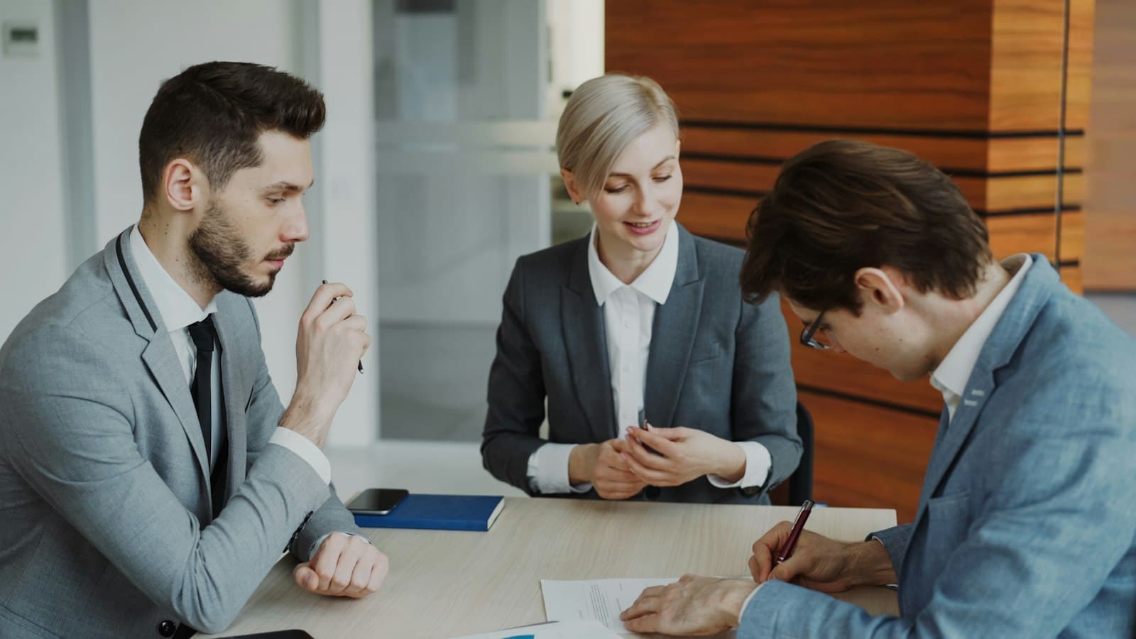 Three colleagues reviewing and signing documents together at a meeting table
